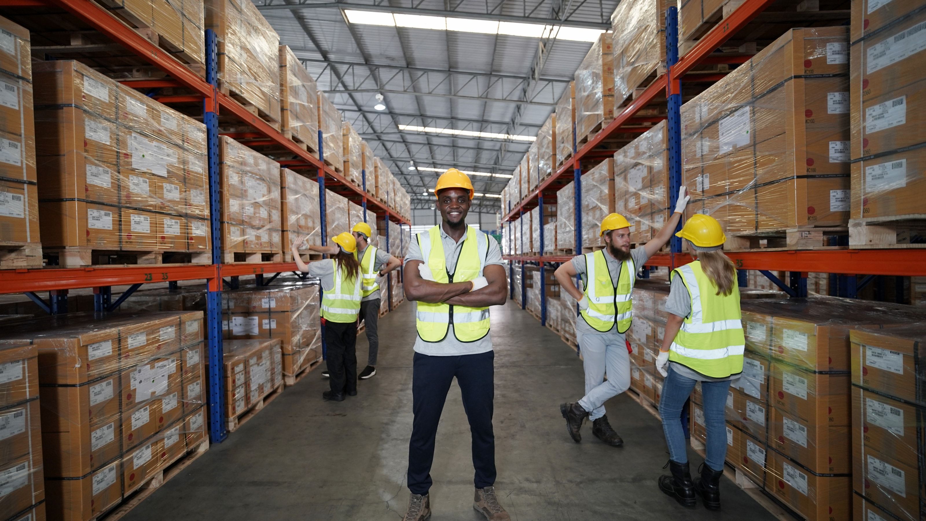 Equipo de almacén con casco y chaleco en el pasillo de un centro de distribución