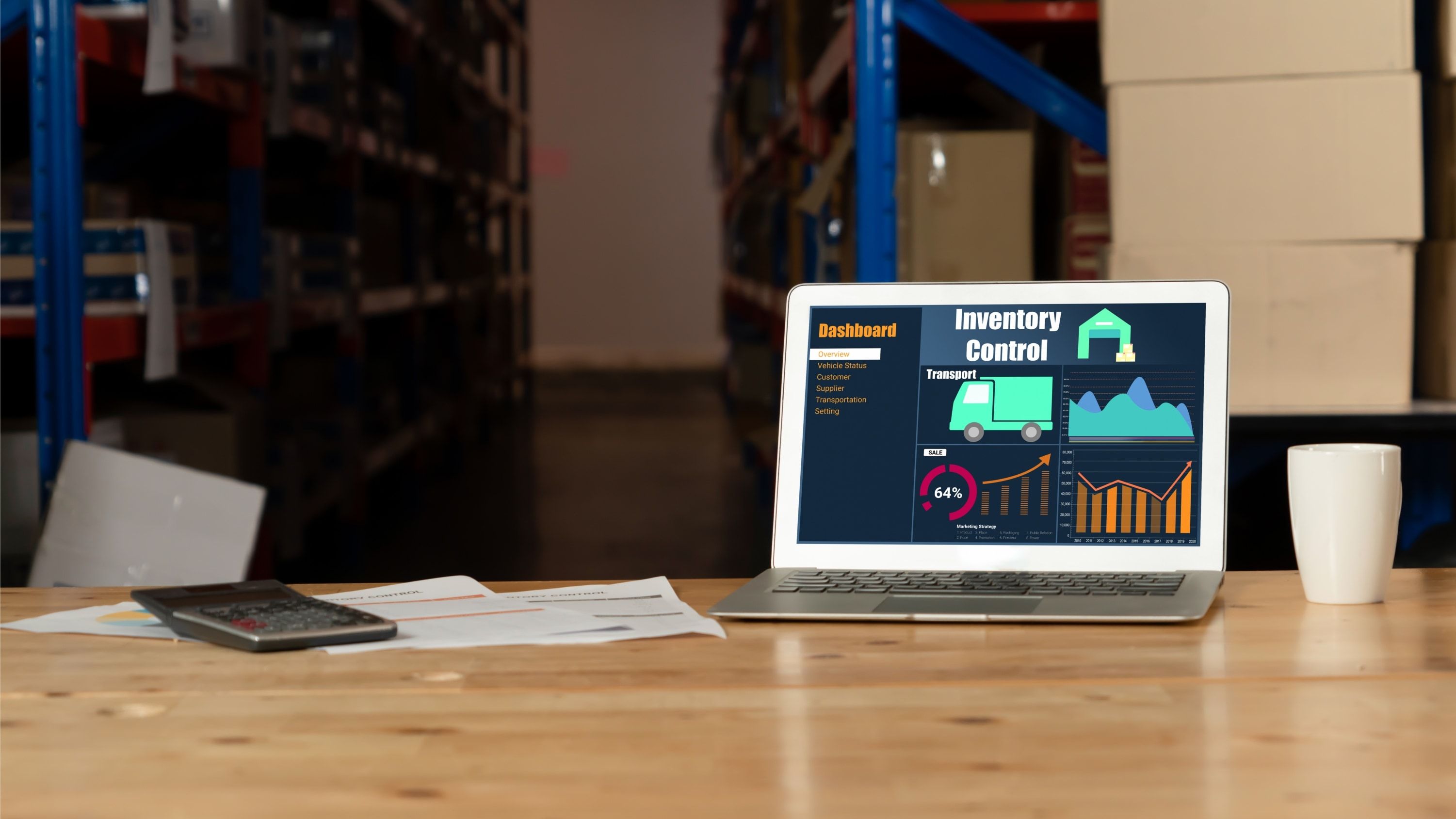 Portátil con un panel de control de inventario sobre una mesa de trabajo en un almacén